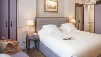 A hotel room with a large bed, two bedside lamps, a nightstand, a framed picture on the wall, and a suitcase on the floor.