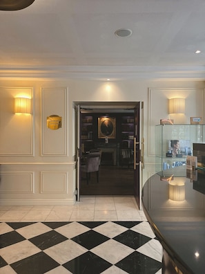 A hotel lobby with a checkered floor, a reception desk, and a bookshelf with books. - Hôtel de Sèze (Bordeaux)