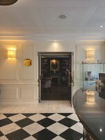 Una hall d'albergo con pavimento a scacchi, una reception e una libreria piena di libri.
