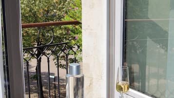 A glass table with a wine glass, a bottle, and a book on a balcony with a view of buildings and trees.