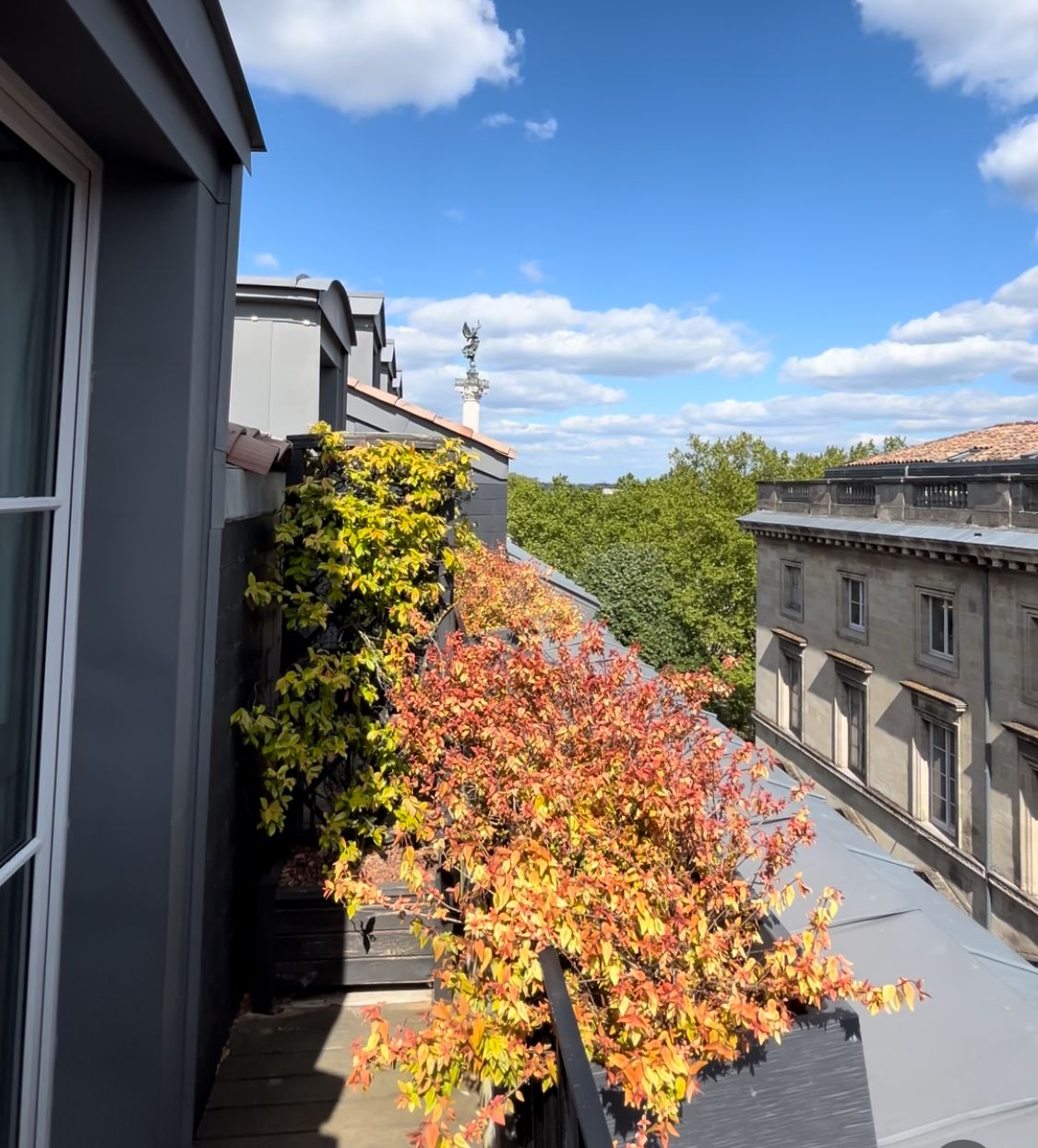Un bâtiment à la façade grise, doté d’une cheminée visible et d’un balcon orné de feuillage d’automne.