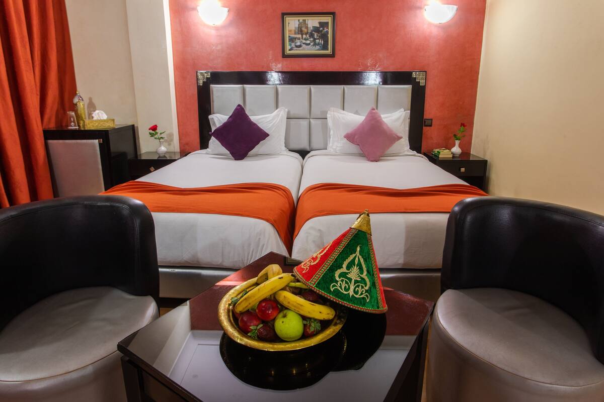 A hotel room with two beds, a fruit basket, and two chairs.