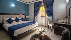 Une chambre d’hôtel avec un grand lit, un bureau, une chaise et une fenêtre avec des rideaux bleus.