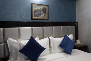 A hotel room with a bed, white and blue pillows, a headboard, a framed painting on the wall, and a nightstand with a tissue box. - Hôtel Meriem (Marrakech)