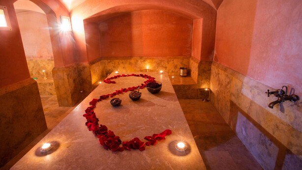 Un couloir à la lumière tamisée, doté d’une voûte en arc, où se trouve une longue table surmontée de marbre, parsemée de pétales de rose et illuminée de bougies, ce qui évoque une atmosphère romantique ou propice à une cérémonie.