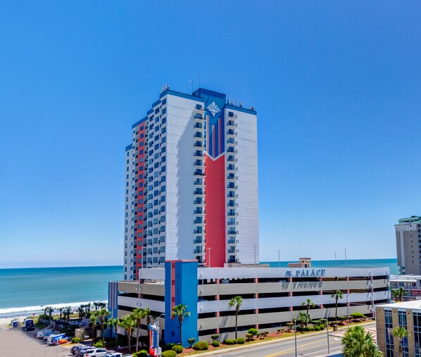 A tall hotel with a prominent red and blue vertical stripe, located near a beach with a parking garage in front. - Palace Resort (Myrtle Beach)