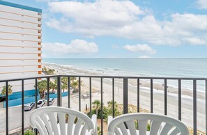 A balcony with white chairs overlooking a beach with a clear sky and ocean. - Palace Resort (Myrtle Beach)