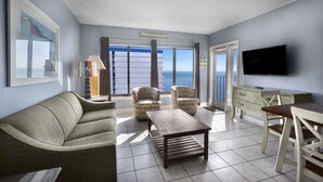 A living room with a sofa, two armchairs, a coffee table, a TV, and a balcony with a view of the sea. - Palace Resort (Myrtle Beach)