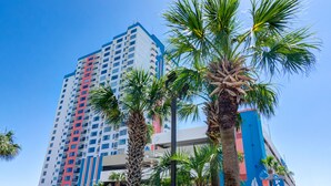 A tall hotel with a red and blue facade, surrounded by palm trees. - Palace Resort (Myrtle Beach)
