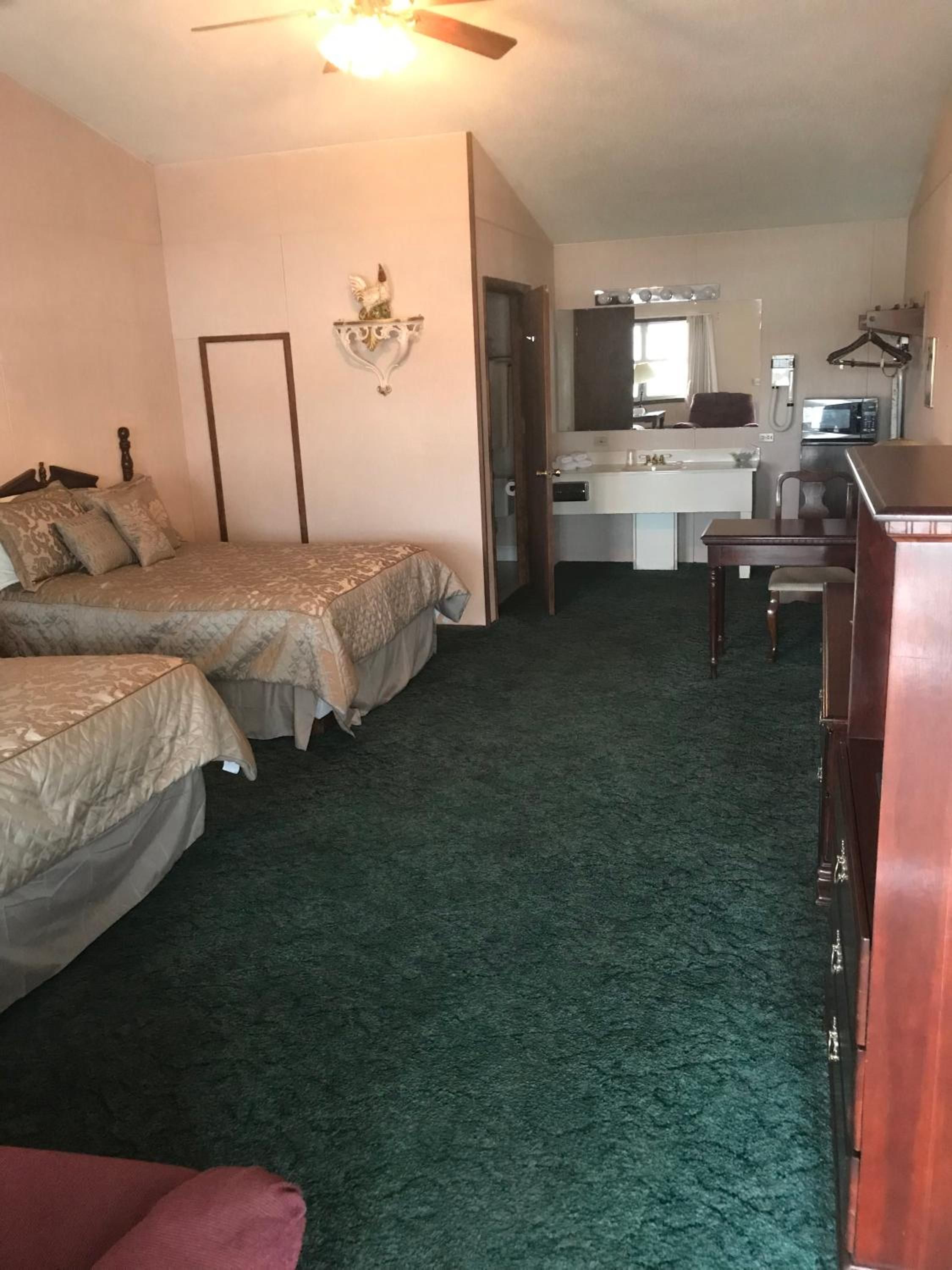 A hotel room with two beds, a desk, a chair, a microwave, and a ceiling fan.
