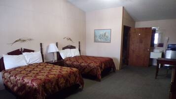 A hotel room with two single beds, a desk with a chair, a lamp, and a painting on the wall.