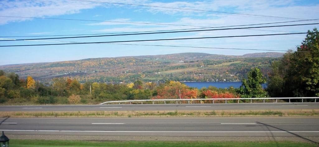A road with a guardrail and a view of a lake surrounded by hills.
