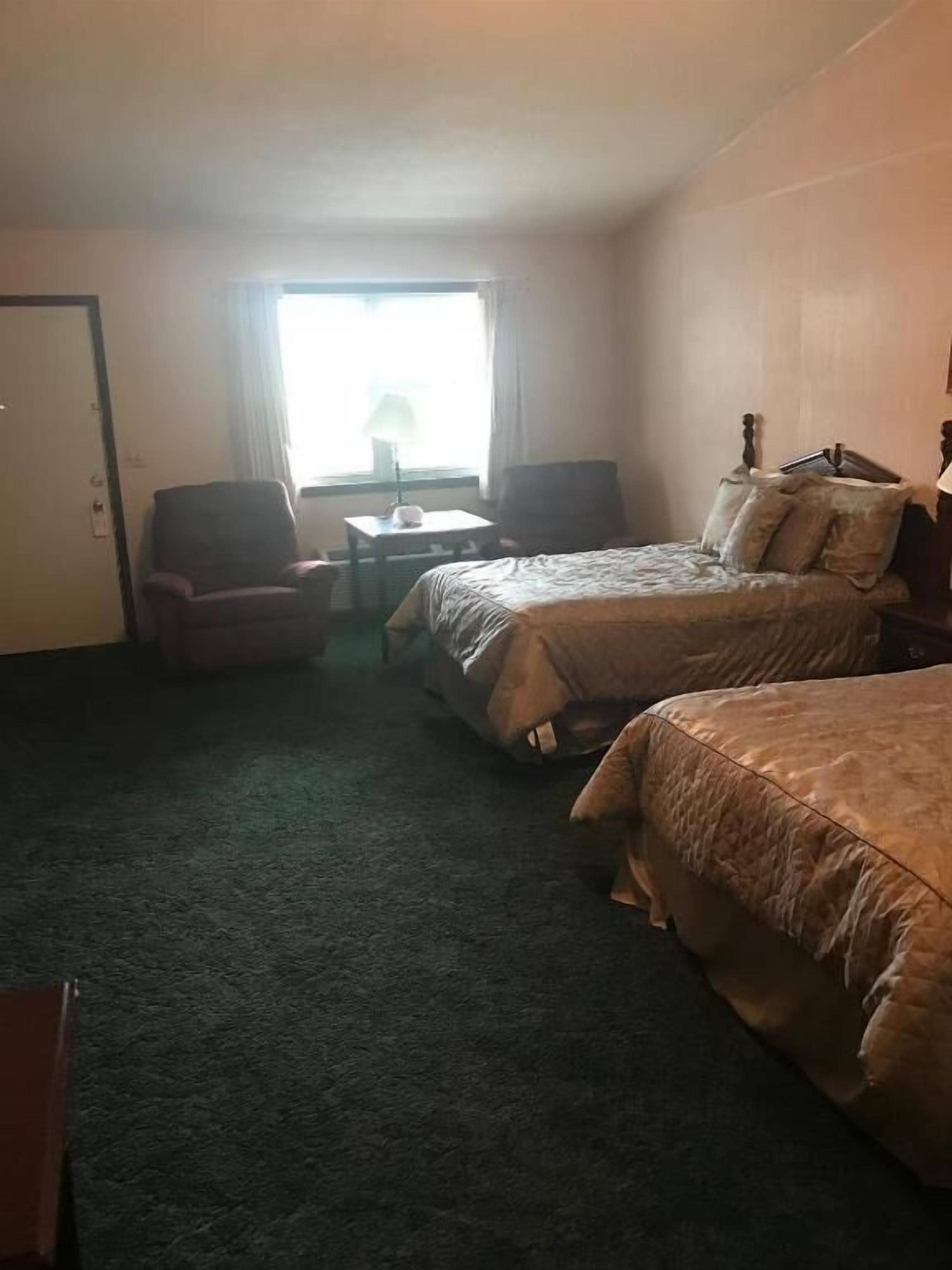 Une chambre d’hôtel avec deux lits, une petite table, deux chaises et une fenêtre avec des rideaux.