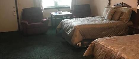 Une chambre d’hôtel avec deux lits, une petite table, deux chaises et une fenêtre avec des rideaux.