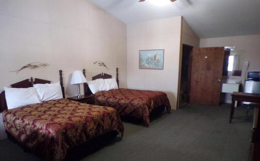 A hotel room with two beds, a desk, a chair, a lamp, and a painting on the wall.
