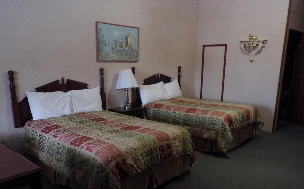 A room with two single beds, a nightstand with a lamp, a painting on the wall, and a decorative wall piece.