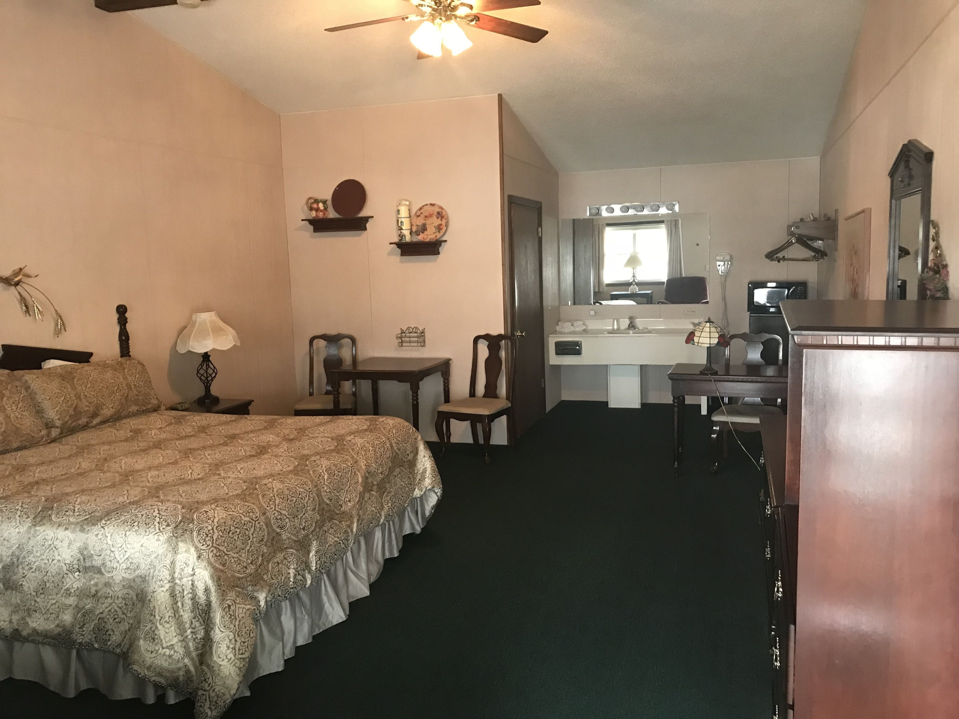Habitación de hotel con cama, escritorio, silla, cómoda, tocador con espejo y ventilador de techo.