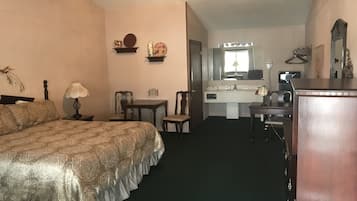 Habitación de hotel con cama, escritorio, silla, cómoda, tocador con espejo y ventilador de techo.