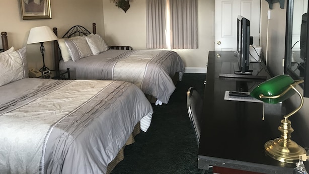 A hotel room with two beds, a desk with a computer, a ceiling fan, and a window with curtains.