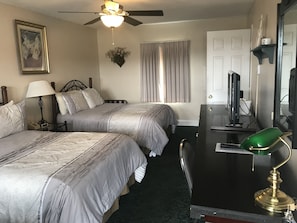 A hotel room with two beds, a desk with a computer, a ceiling fan, and a window with curtains. - Longhouse Lodge Motel (Watkins Glen)