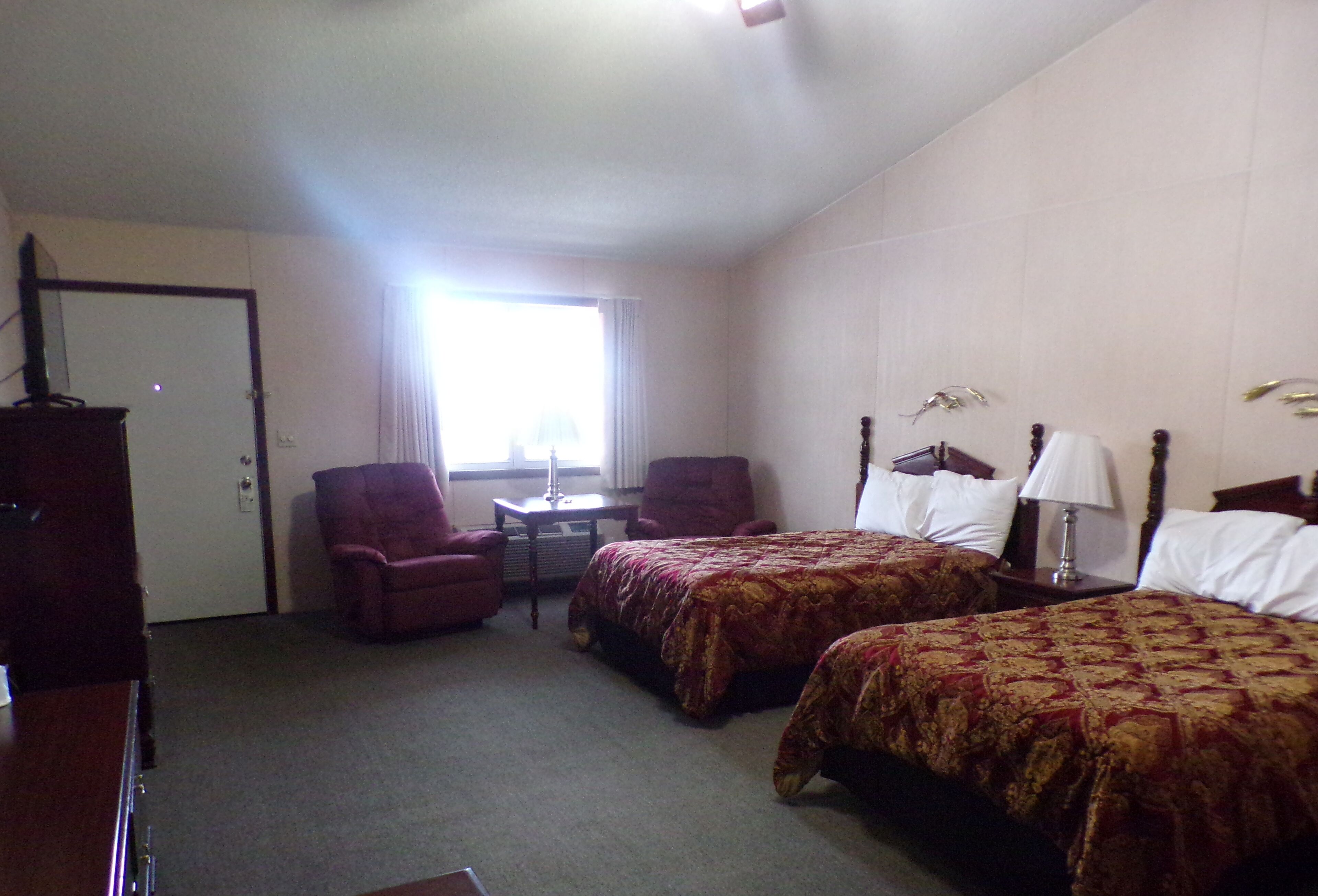 A hotel room with two beds, a desk, a chair, and a wardrobe.