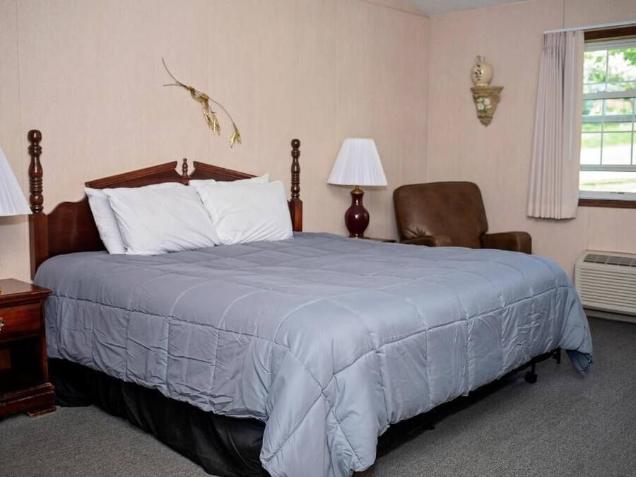 A hotel room with a large bed, two bedside tables with lamps, a chair, a wall-mounted lamp, and a window with curtains.