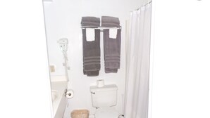 A small, white bathroom with a toilet, a trash bin, and a towel rack with two towels.