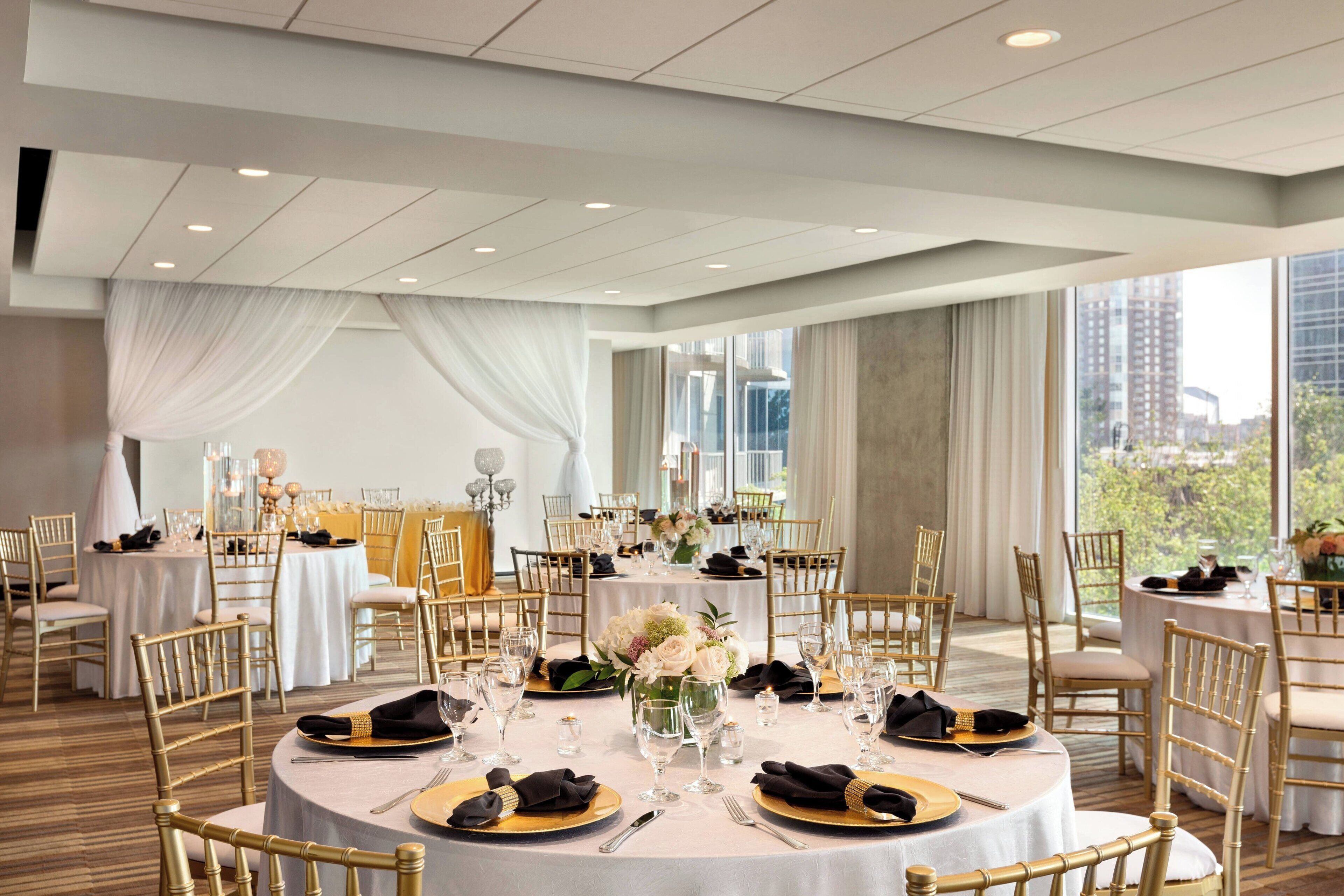 A banquet hall with round tables, gold chairs, and white tablecloths.