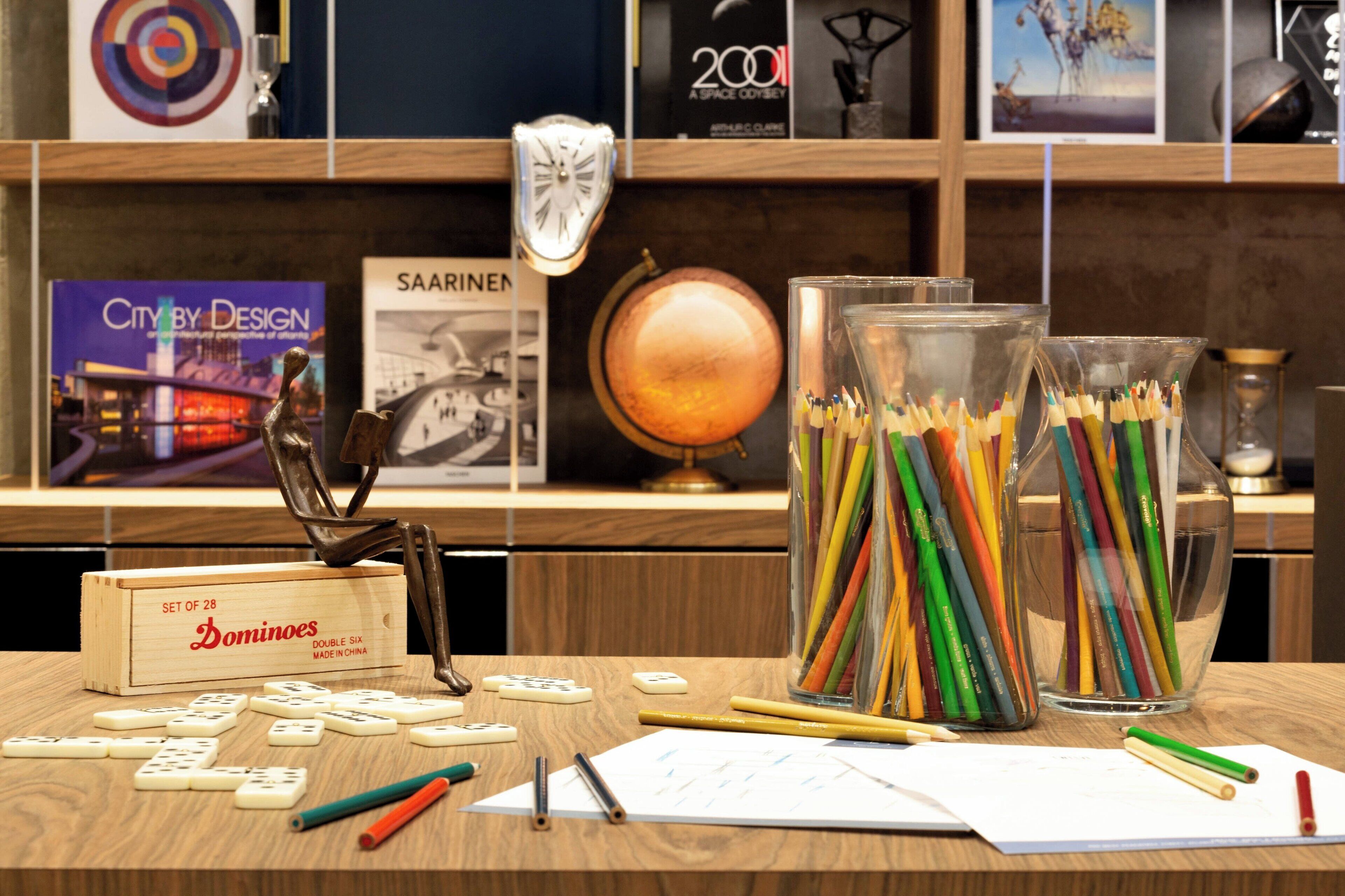 A desk with dominoes, pencils, and a glass jar filled with colored pencils.