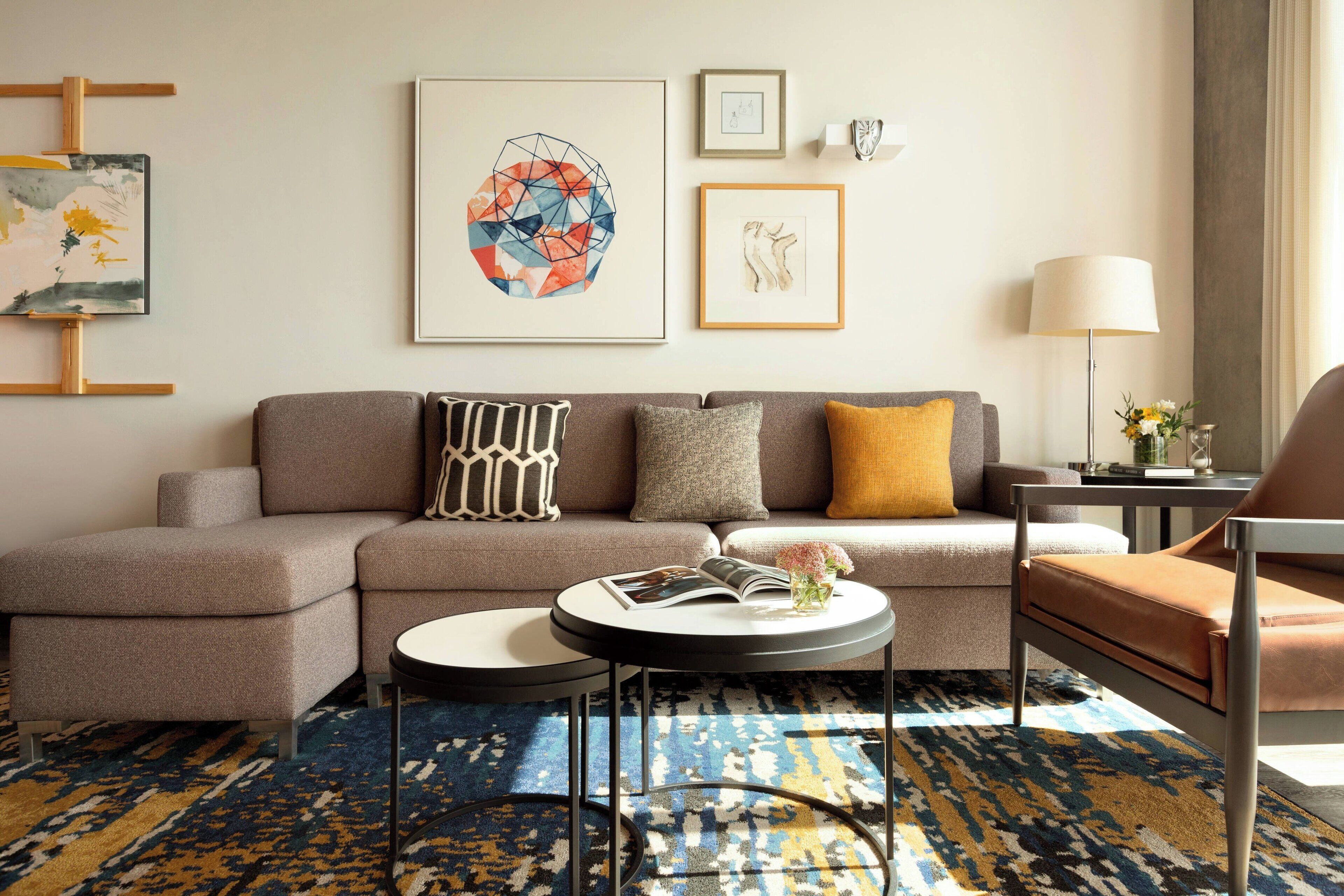 A modern living room with a sofa, coffee table, and armchair. There are framed artworks on the wall and a lamp on a side table.