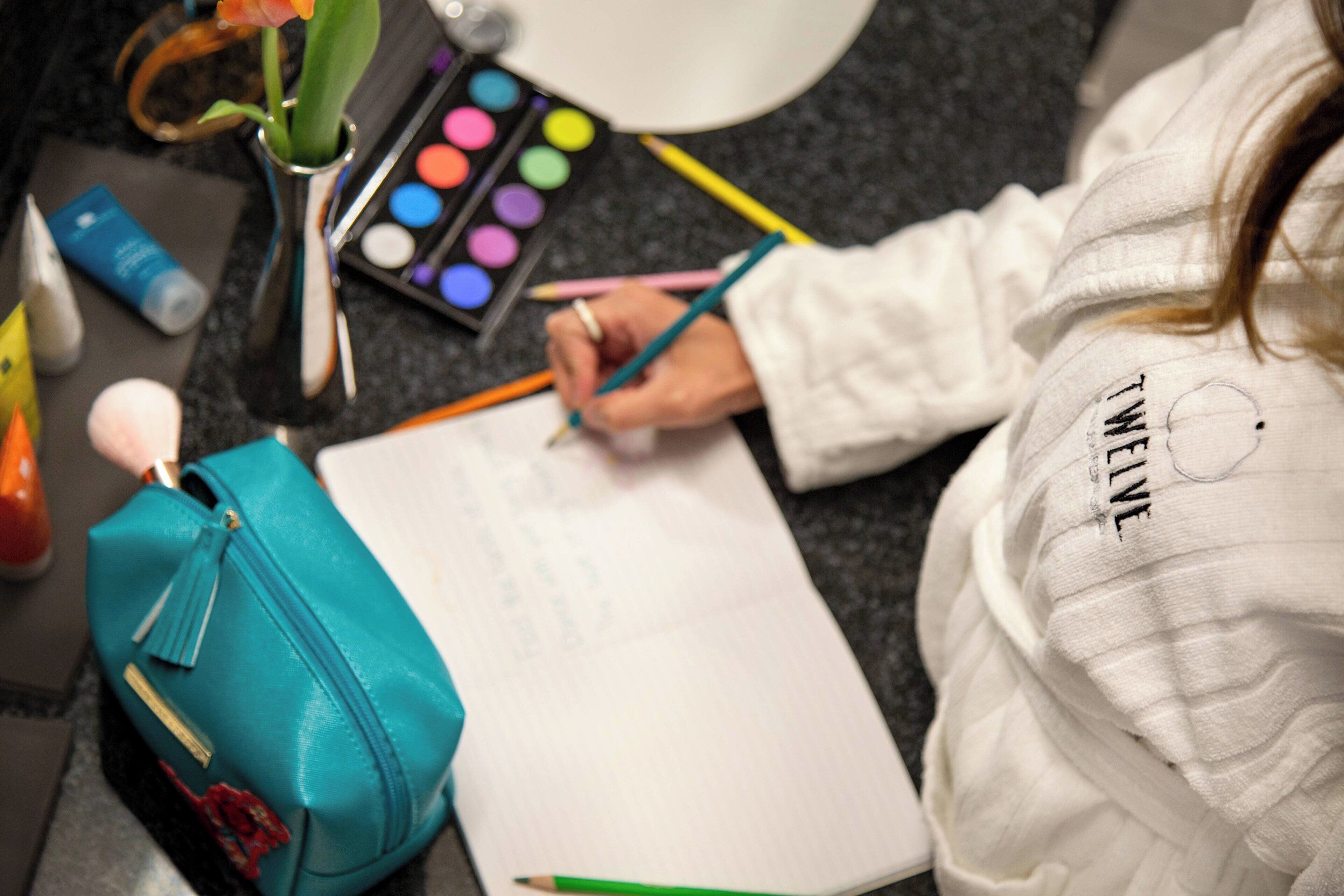 A person writing in a notebook with a teal bag beside them.