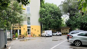 Un hotel con fachada amarilla, mesas al aire libre y un estacionamiento con coches.