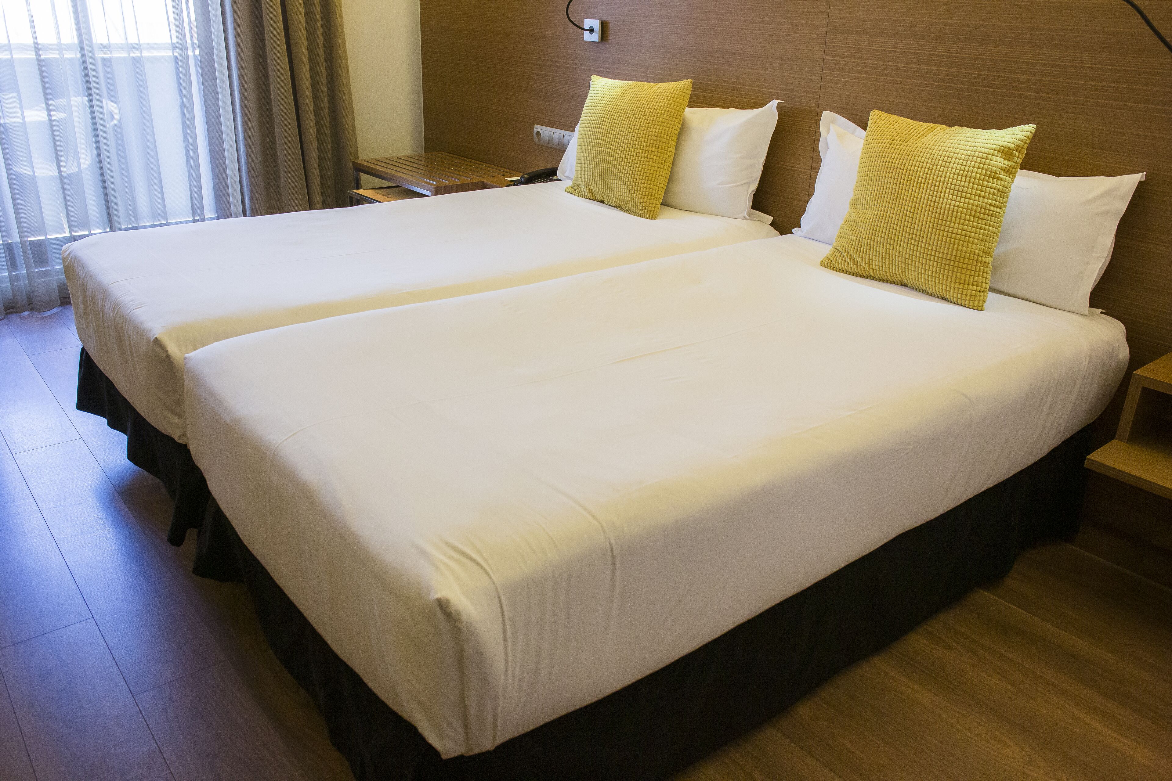 Ett hotellrum med två sängar, en sänggavel i trä och ett litet bord.