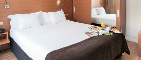 Una habitación de hotel moderna con una cama grande, una mesita de noche con un teléfono, un espejo y una bandeja de desayuno sobre la cama.