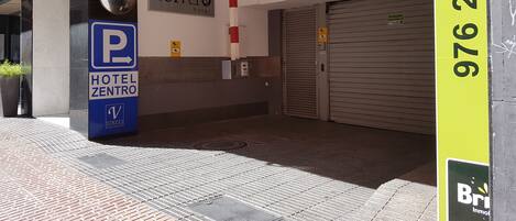 Entrada de hotel con señal de estacionamiento, cartel con el nombre del hotel y un número de contacto.