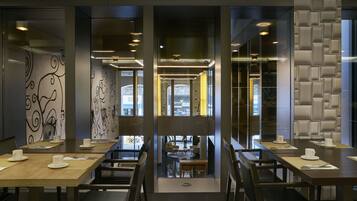 A modern restaurant with a central dining area, glass partitions, and a view of the street.