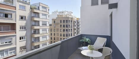 A balcony with a small table and chairs, potted plants, and a view of surrounding buildings.
