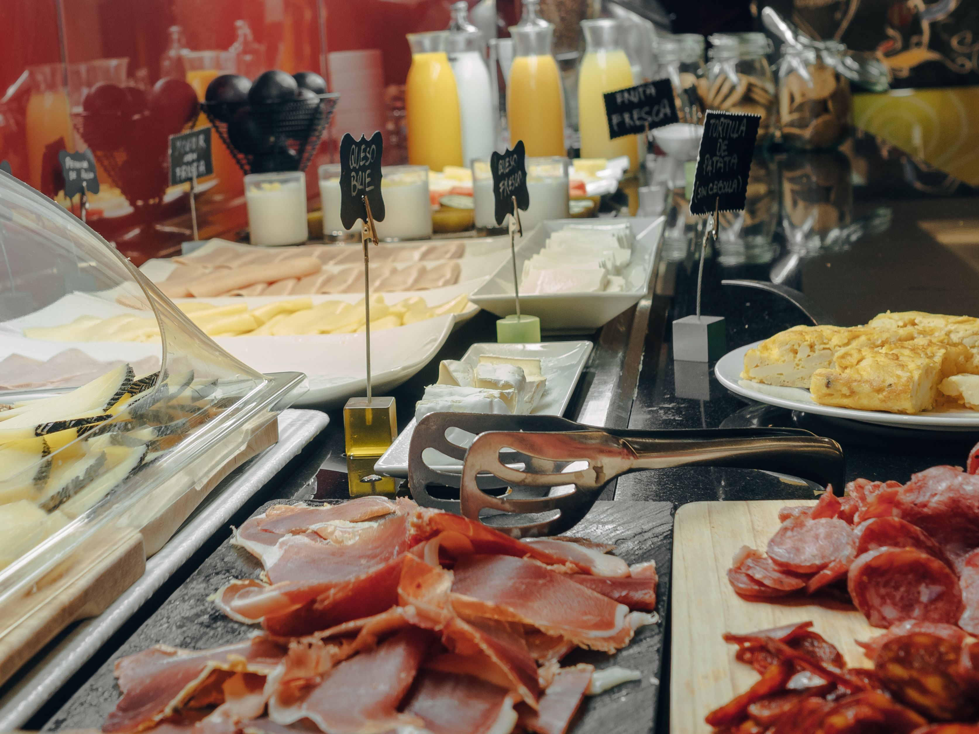 A breakfast buffet with various food options including meats, cheeses, and fresh fruits.