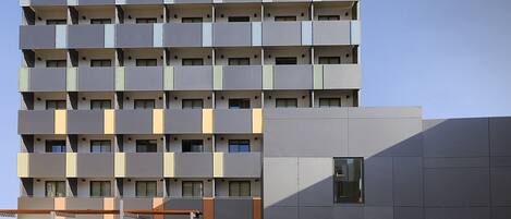 Un edificio de varios pisos con un diseño arquitectónico moderno, que cuenta con balcones y un techo plano.
