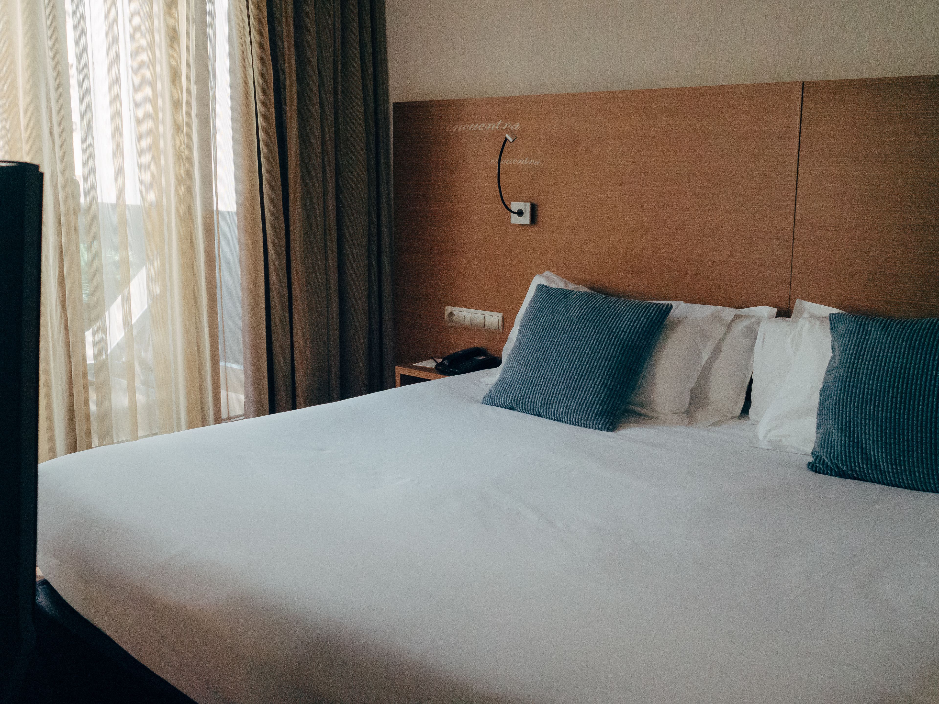 Une chambre d’hôtel avec un grand lit, une tête de lit en bois et un téléphone sur une table de chevet.