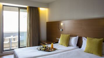 Habitación de hotel con cama, bandeja de desayuno, mesita de noche, silla y vista al exterior.