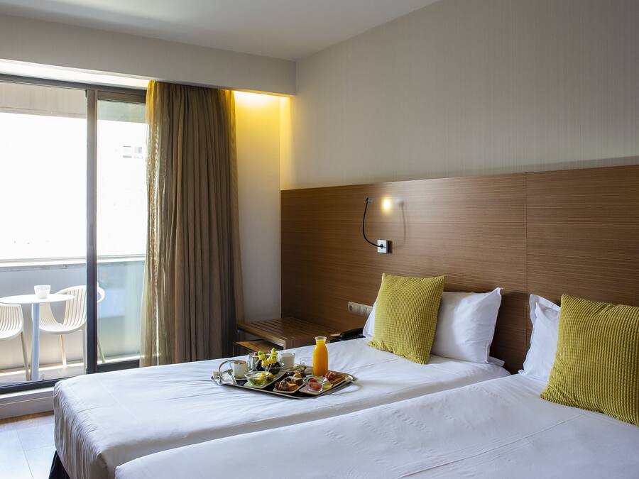 Habitación de hotel con cama, bandeja de desayuno, mesita de noche, silla y vista al exterior.