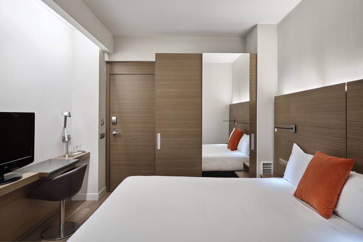 Een moderne hotelkamer met een bed, een bureau met een televisie, een stoel en een kledingkast.