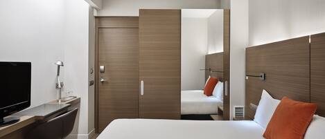 Una habitación de hotel moderna con cama, escritorio con televisor, silla y armario.