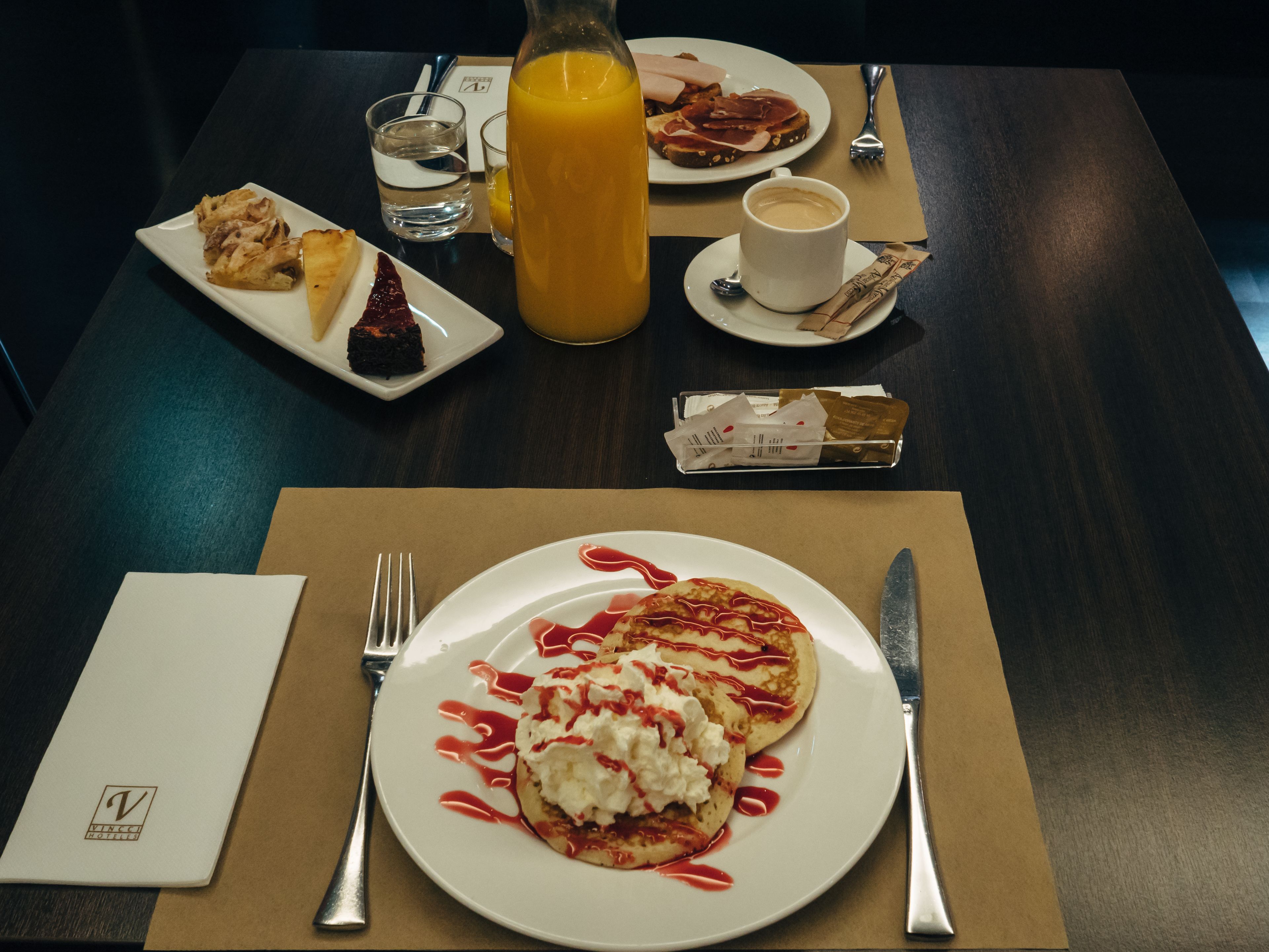 A breakfast setting with pancakes, a glass of orange juice, a cup of coffee, and a plate of ham and cheese.