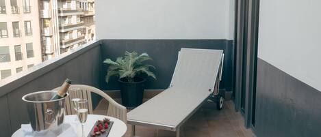 Ein Balkon mit Tisch, Stuhl, Liegestuhl, einem Topfpflanzen und einer Champagnerflasche.