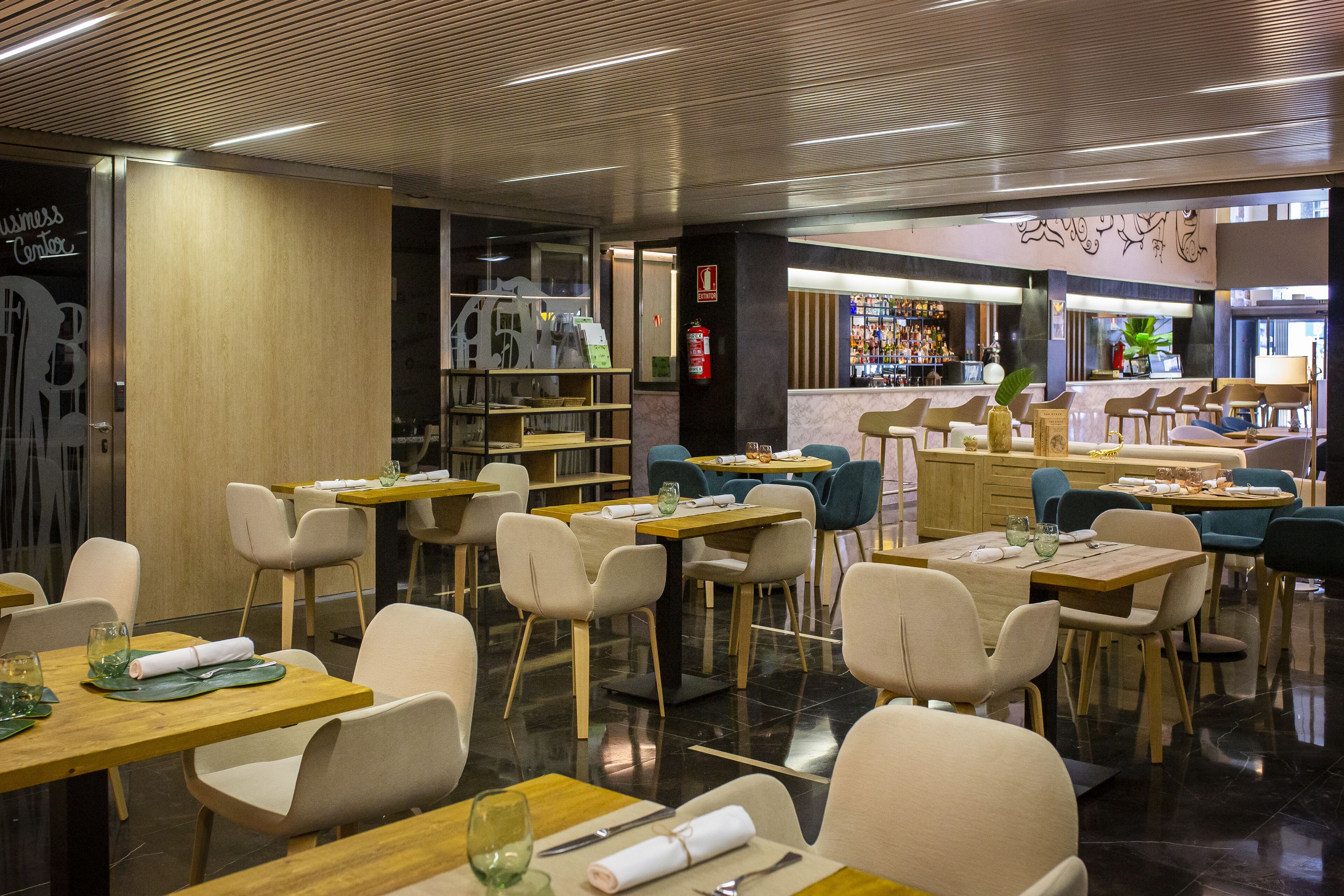 A restaurant with multiple tables and chairs, a bar area, and a counter with a variety of items.
