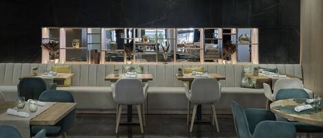Un restaurante moderno con una zona de estar central, mesas individuales y vistas a la cocina a través de un ventanal grande.