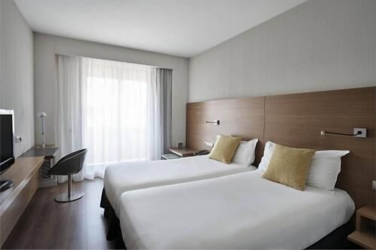 Een hotelkamer met twee bedden, een bureau, een stoel en een groot raam met gordijnen.