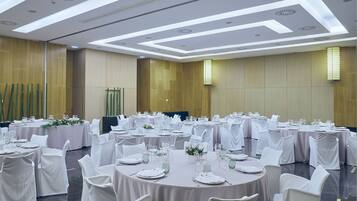 Uma sala de banquetes com mesas redondas preparadas para refeições, cadeiras brancas e um design de teto moderno.